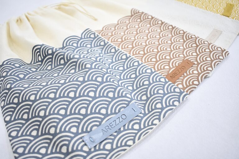 Em algodão 100% cru, bainha especial, cordoaria tinturada em Pantone específico e silk e aplicação de etiqueta.